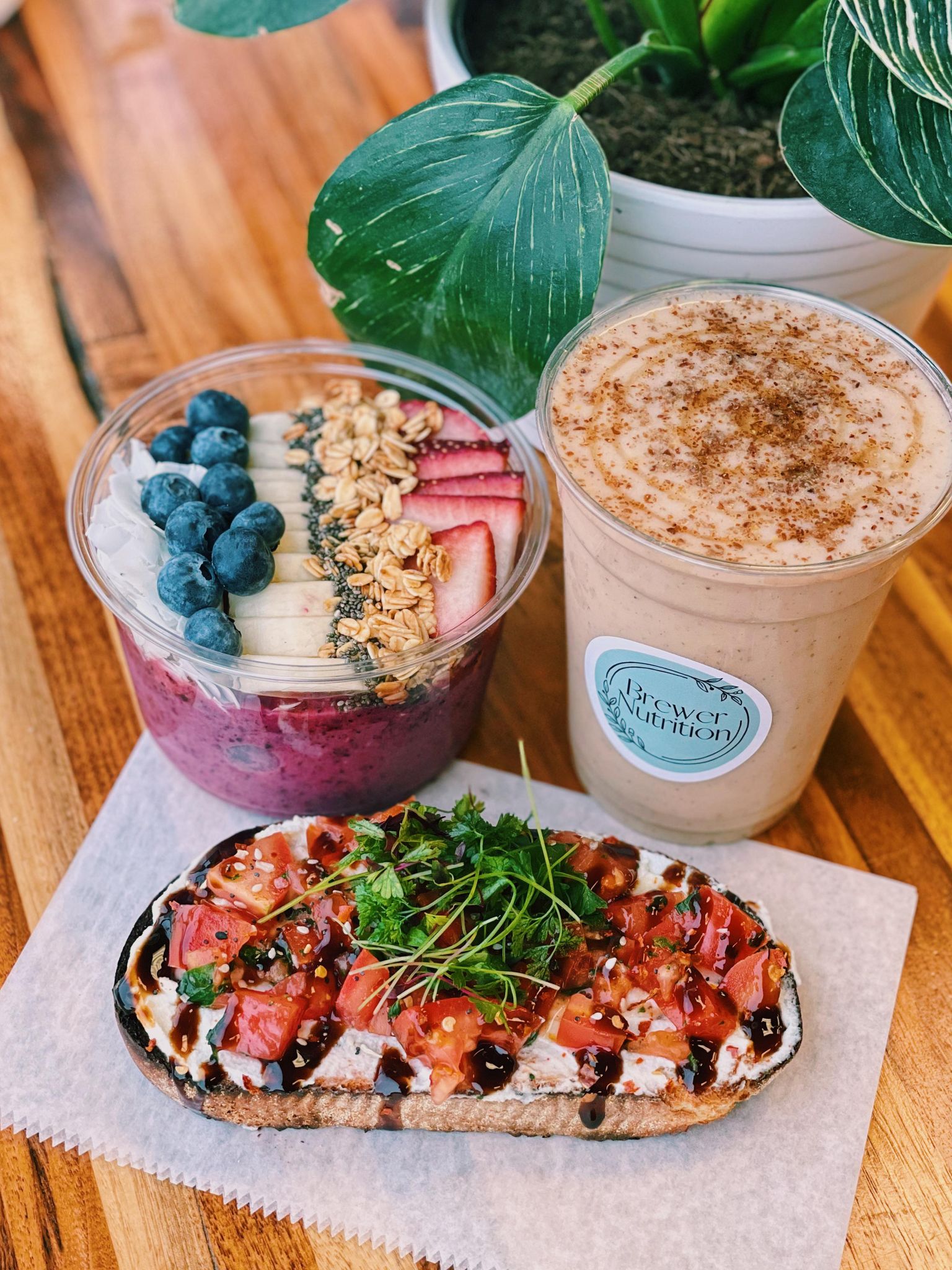An açaí bowl topped with blueberries, banana, granola and strawberries beside a smoothie and tomato toast