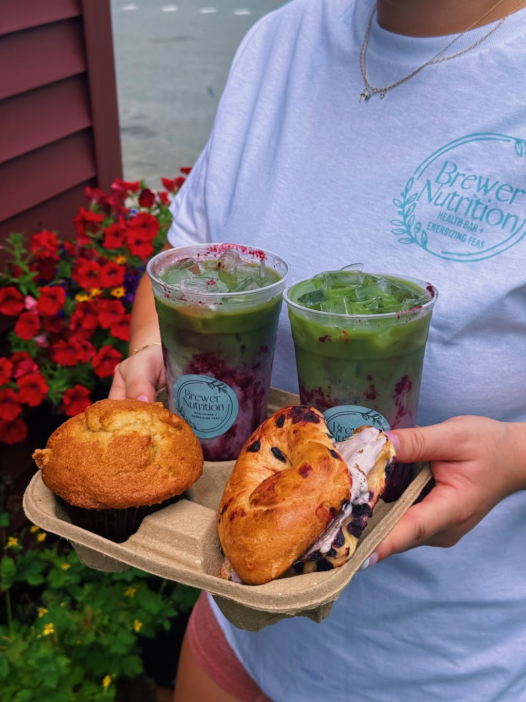 A carry tray with two green energizing teas, a muffin and a berry bagel, held outside the shop